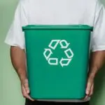 Adult male holding a green recycling bin against a green background, promoting sustainability.
